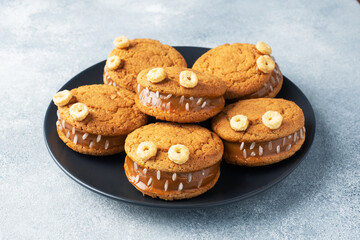 Cookies with cream paste in the shape of monsters for Halloween celebration. Funny homemade faces made of oatmeal cookies and boiled condensed milk.