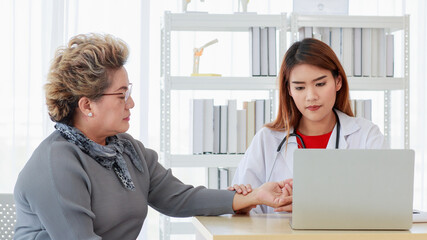 Focus to asian senior elderly woman wearing sphygmomanometer to measuring blood pressure and doctor woman carrying stethoscope on neck and hold her hand to older patient in examination room