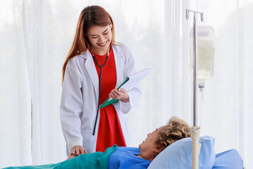 Asian woman doctor smiling while holding senior elderly woman patient hand to support encouragement and talking look comfortable. Patient sleep on bed in examination room at hospital