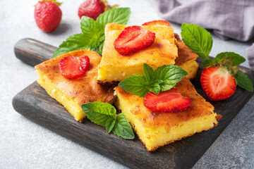 Cottage cheese casserole with strawberries and mint. Delicious homemade dessert made of curd and fresh berries with cream. Gray concrete background close up.