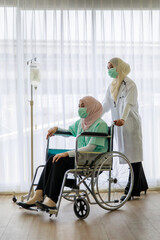Fototapeta na wymiar Young female muslim doctor wearing face mask pushing the wheel chair of young sick muslim pateint in hospital