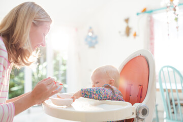 Mother feeding baby girl in high chair