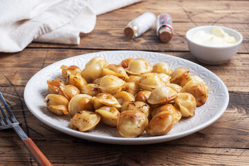 Traditional fried pelmeni, ravioli, dumplings filled with meat on plate, russian kitchen. Wooden rustic table, copy space.