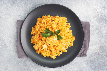 Delicious Asian pilaf, stewed rice with vegetables and chicken on a plate. gray concrete background.