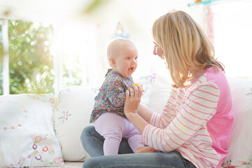 Mother playing with baby girl on sofa