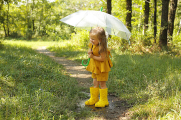 a beautiful blonde girl in a mustard-colored linen suit with a transparent umbrella stands in the rain in the park
