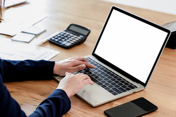 Businesswomen hand on mockup laptop keyboard with blank screen on the desk.