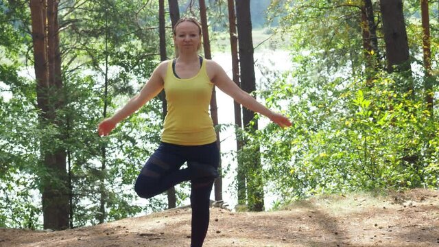 Young woman doing yoga in morning park near lake. a sports girl with a beautiful figure goes in for sports in nature, in sportswear. doing exercises. poses, assanas, stretching. strengthening muscles.