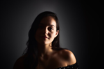 Close-up portrait of a young woman with a positive gaze looking at the camera, on a dark studio background