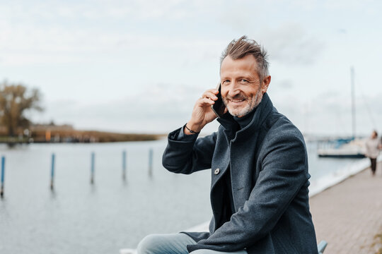 Senior man relaxing at a marina taking a call on his mobile - Powered by Adobe