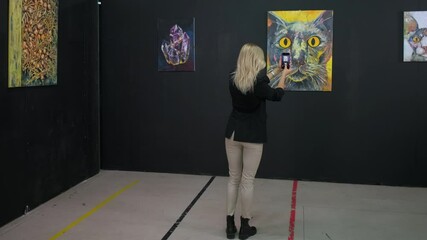female visitor of fine art museum is photographing picture by smartphone