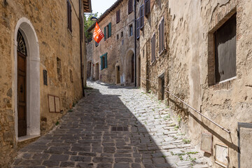 Fototapeta na wymiar A narrow medieval stone paved street with a red waving flag in the tuscanian town of Montalcino