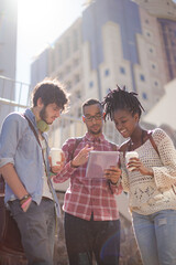 Friends using digital tablet on city street