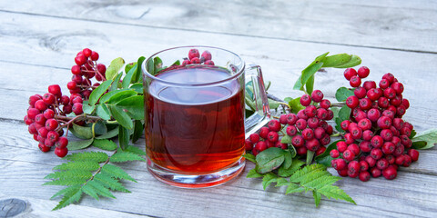 Mug with tea, sunflower flower and rowan berries on a wooden background. Black tea in a glass cup.