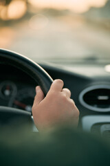 Selective focus of man's hand on steering wheel, driving a car at sunset. Travel background with copy space area.