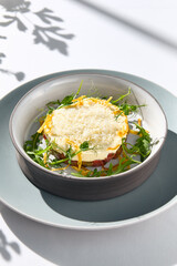 Beef tartare under cheese sauce with deep fried onion. Fancy dinning with beef tartare on white table with simple contemporary decoration. Sunlight and harsh shadow still life. Beef tartare blue dish.