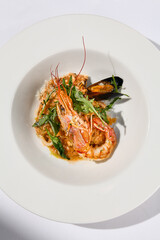 Risotto with seafood in contemporary style on white background. Italian risotto with prawn, mussels, squid in frutti di mare style. Summer dining with seafood and rice. Summer day seafood concept.