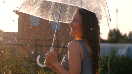 Portrait of a beautiful girl with umbrella in the sunset smiling during rain at sunny day
