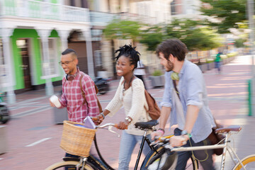 Friends pushing bicycles on city street