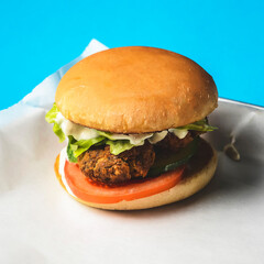 Bacon burger with beef patty, fresh tomatoes and cucumbers with sauce served on a metal tray over white background.
