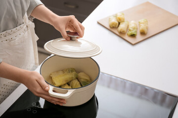 Woman preparing stuffed cabbage rolls on electric stove at kitchen, closeup