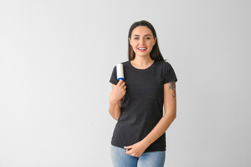 Young woman with lint roller on light background