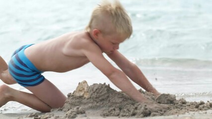 Little blonde boy playing with sand on ocean beach sea. Angry upset kid breaks sand castle. Family summer holidays and trips to warm countries - Powered by Adobe