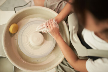 Crop craftswoman shaping pot on wheel