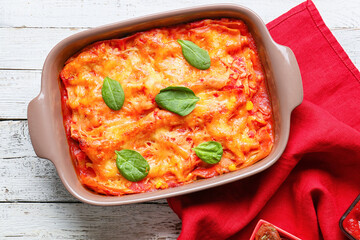 Baking dish with tasty tomato lasagna on light wooden background