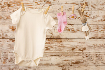 Baby clothes, pacifier and toy hanging on rope against light wooden background
