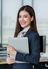 Portrait of young attractive Asian female office worker in formal business suits  smiling at camera in office with blurry office as background