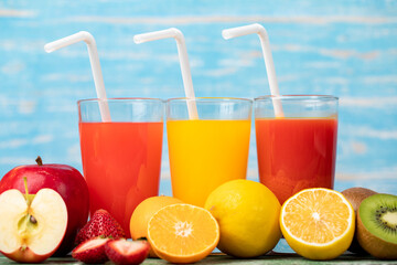 Different fruits juice in glass, apple, orange and strawberry juice with straw, looking refreshing on colourful wood board in front of blue wall background. Picture decorating with fresh fruits