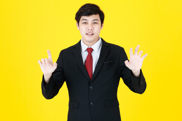 Horizontal portrait shot of young adult Asian handsome man in a black long sleeve suit raising hand up and try to count and calculate the number with his fingers in the studio with yellow background