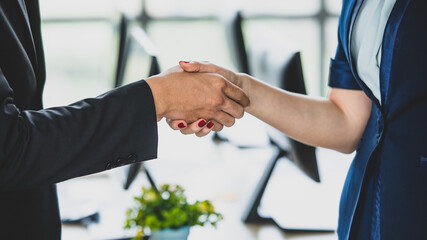 Close-up handshake of two businesspeople in modern office. Businessman and businesswoman shake hand with a computer background. Concept of a business partner, business meeting, and collaboration