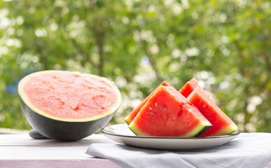 Slices of watermelon on a plate, half a watermelon in the background, outdoor. Healthy food.