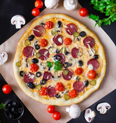 Homemade pizza with salami, mushrooms and cherry tomatoes on a black background. Top view.