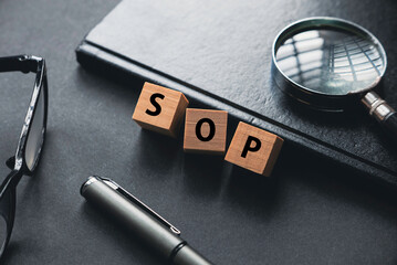 Selective focus of glasses, magnifying glass, notebook, pen and wooden cube written with SOP or Standard Operating Procedure.