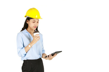 Cute young and beautiful Asian female engineer wearing yellow safety hard hat standing and pose with happy and calm face isolated on white background. She holds tablet computer and cup of coffee