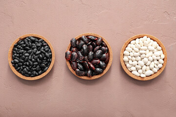 Bowls with raw beans on color background