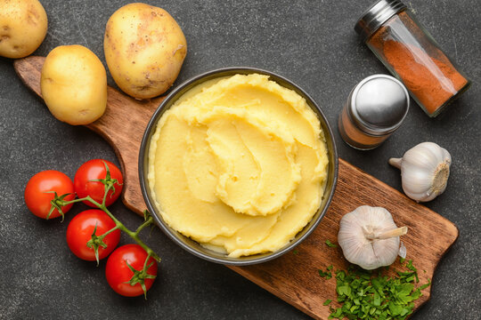 Bowl of tasty mashed potatoes with garlic and vegetables on dark background