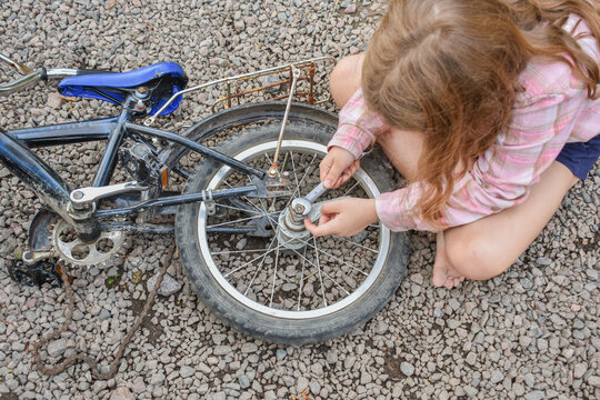 the child girl has damaged a bicycle wheel and is making repairs photo without processing