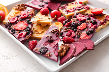 Handmade chocolate bars with fruits, berries and nuts on light background