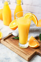 Board with glass of tasty orange juice on light background