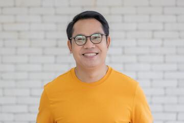 Portrait of adult Asian man wearing  yellow t-shirt and eyeglasses standing and smiling looking to...