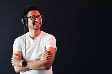 Young African American man wearing headphone, white t shirt and enjoy music over black Background. Red light reflecting on face. Emotions and face expressions