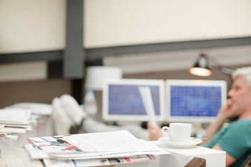 Businessman reading paperwork in office behind coffee cup