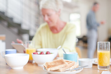 Obraz na płótnie Canvas Older woman using digital tablet at breakfast table