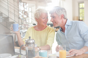 Fototapeta na wymiar Older couple laughing together at breakfast table with laptop