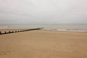 Breakwater leading across sandy beach out to sea on a dull day