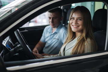 Bussines woman choosing car i car showroom. Salesperson sitting in car with customer and show desing